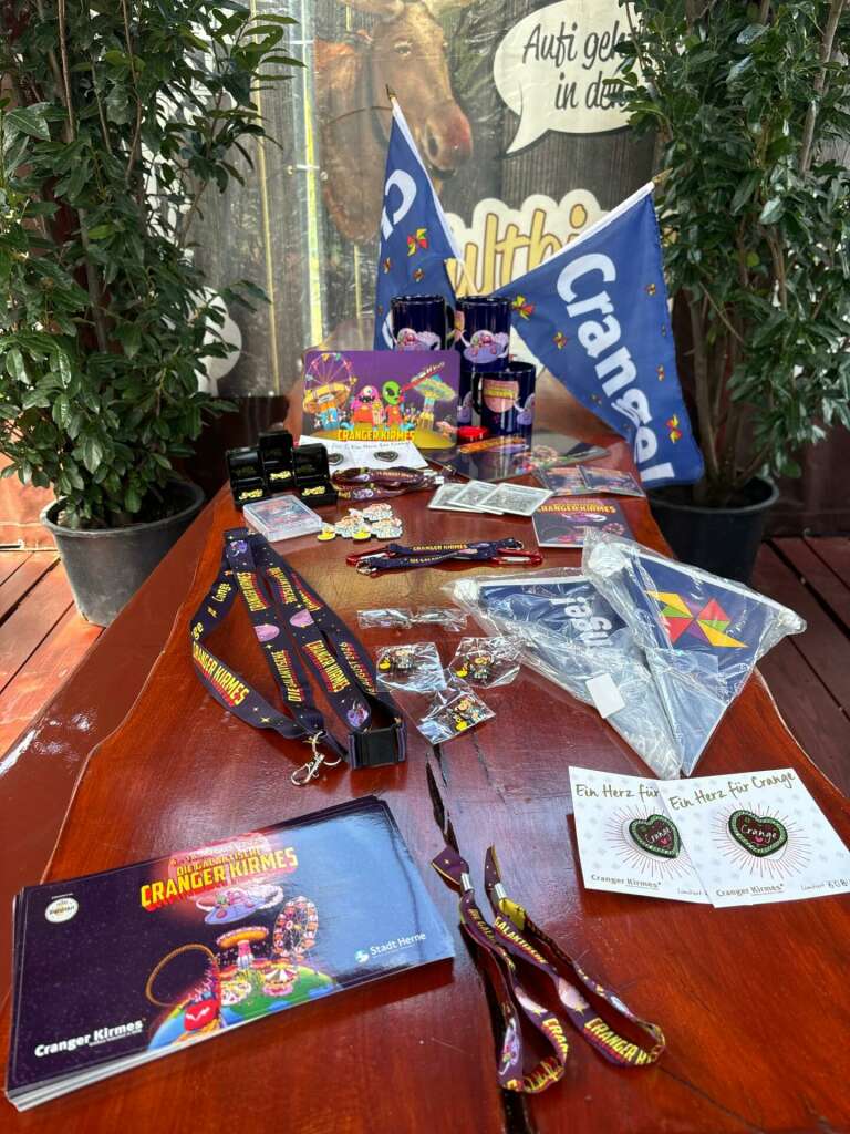 Souvenirs, Souvenirs, Souvenirs: Jedes Jahr bringt das Stadtmarketing Herne für die Cranger Kirmes mit viel Liebe zum Detail und immer frischen Ideen eine neue Andenken-Kollektion heraus. Natürlich mit den beiden absoluten Klassikern, dem Fritz-Pin oder dem Eventband für das Handgelenk, aber auch mit Neuheiten wie einem Herz-Reflektor oder einem Kirmes-Quartett. Neu aufgelegt wurde der vergriffene Pin mit dem unverwechselbaren Windrad-Logo. Die galaktischen Außerirdischen erzählen die Geschichte des aktuellen Kirmesplakats weiter und schmücken zahlreiche Neuheiten der Souvenir-Auswahl des größten Volksfestes in Nordrhein-Westfalen, das am 6. August 2026 beginnt und bis zum 16. August etwa vier Millionen Gäste in seinen Bann ziehen wird.
